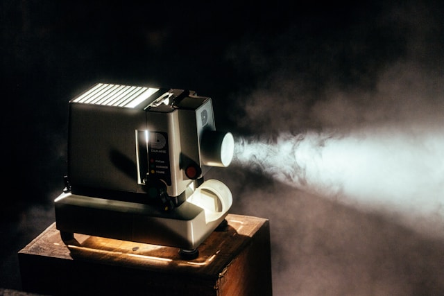Photo of a boxy, old-timey film projector, with fog visible in its bright light.